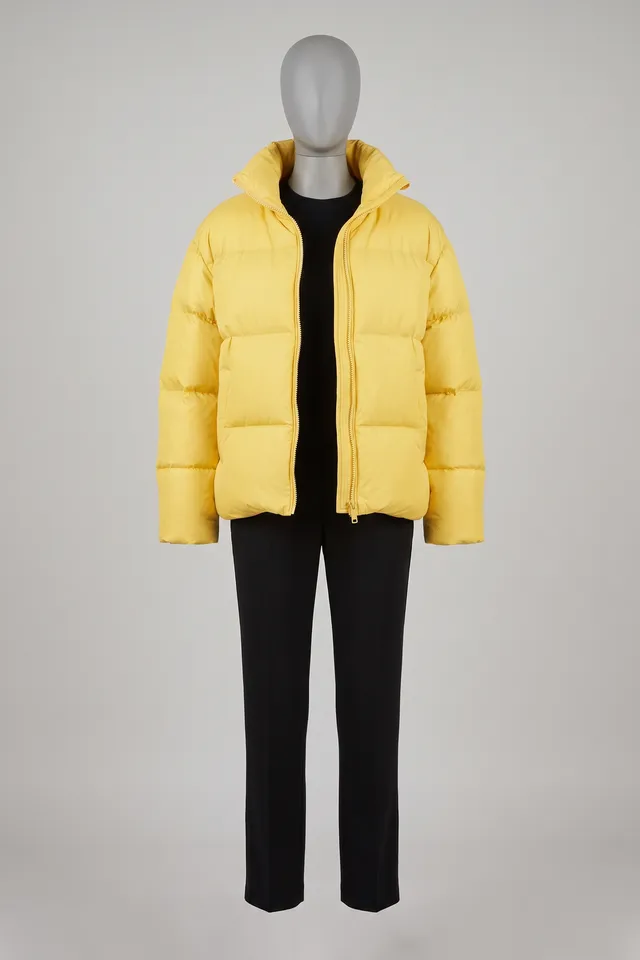 Canary-yellow oversized puffer jacket over black trousers on a headless dress form
